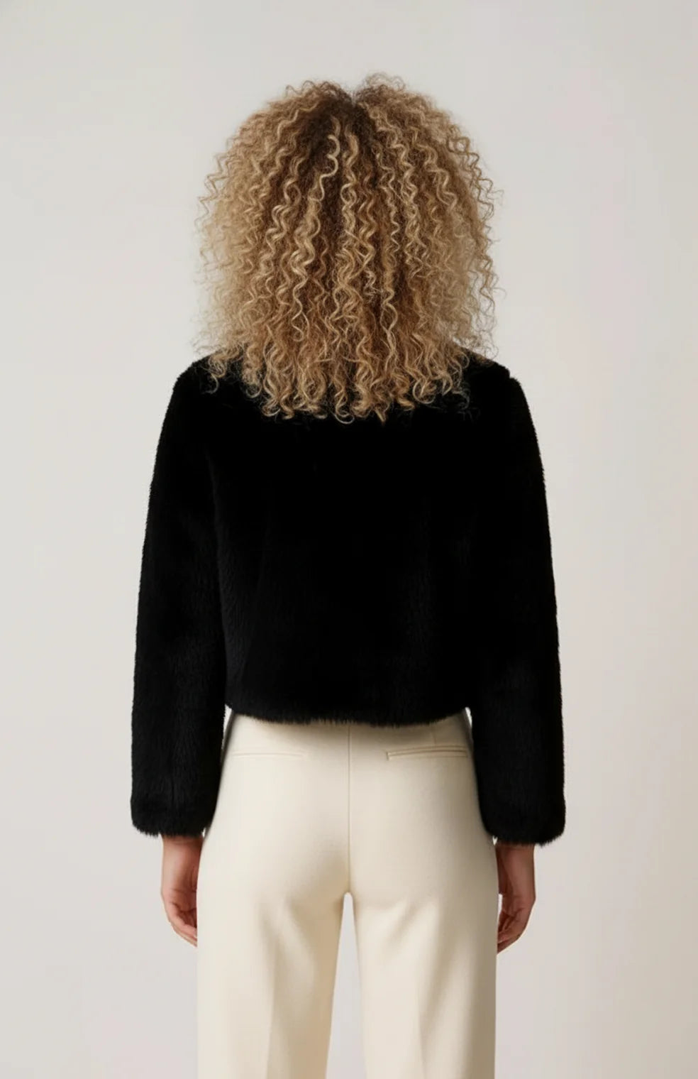 A cropped black women's furry jacket with an open front, rear view