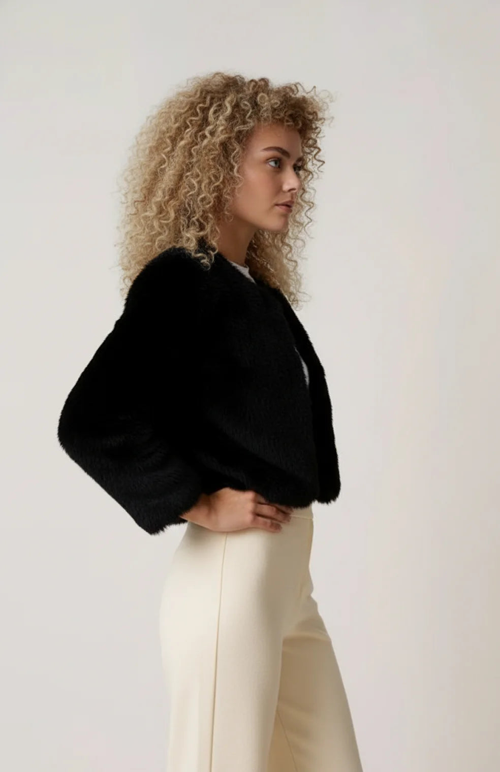 A cropped black women's furry jacket with an open front, side view