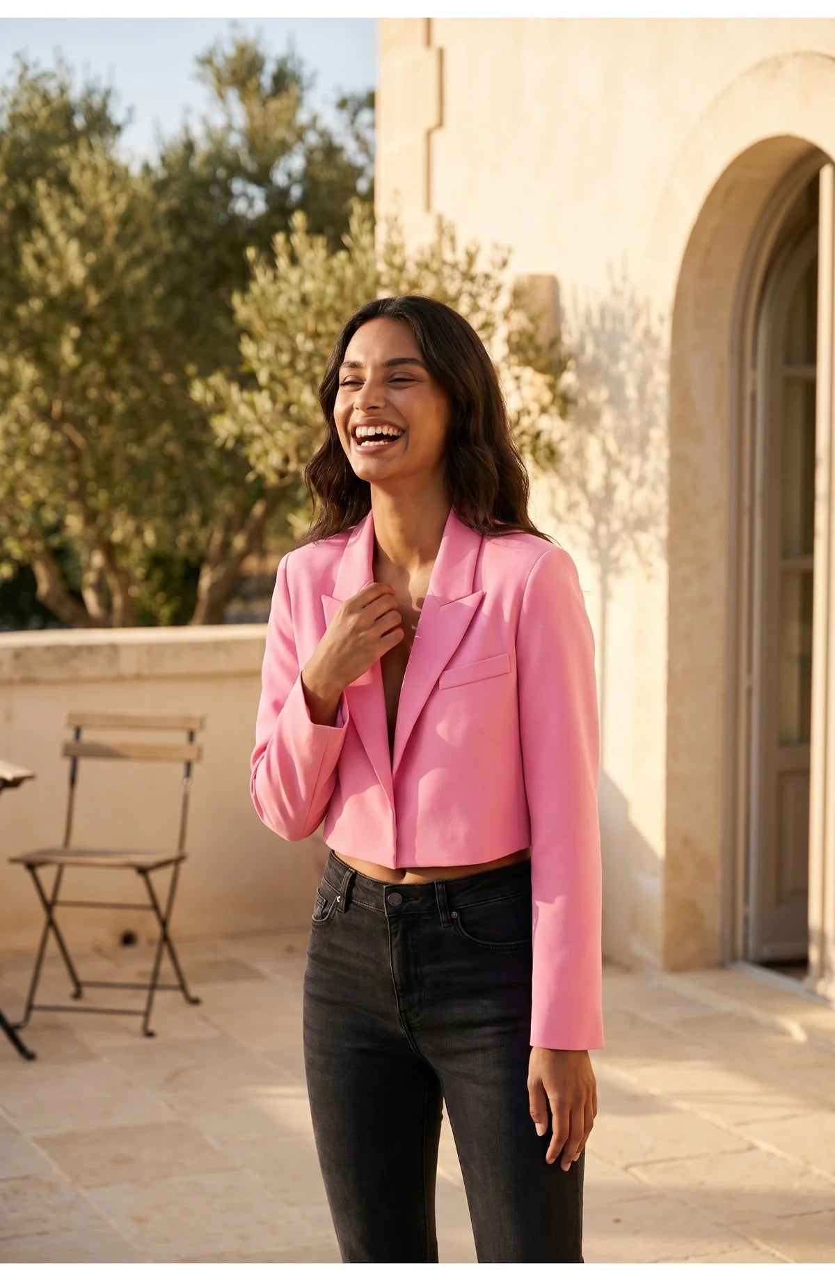 A cropped pink blazer with long sleeves and lapels, worn with black trousers