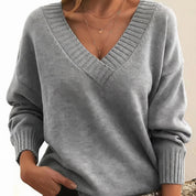 A light-grey women's knitted V-neck jumper with long sleeves and ribbed trims