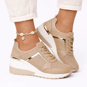 A beige women's wedge trainer with laces, gold metallic panels and perforations