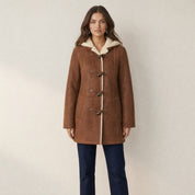 Model in bruine suède-look winterjas met teddyvoering, capuchon en houtjes-touwtjessluiting