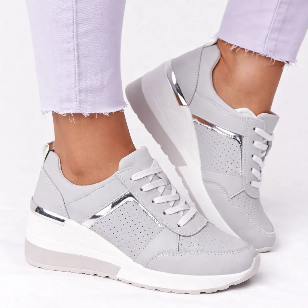 A grey women's wedge trainer with laces and a metal heel accent