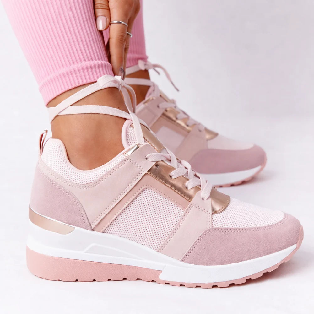 A pink women's wedge trainer with laces, perforations and a metallic side panel